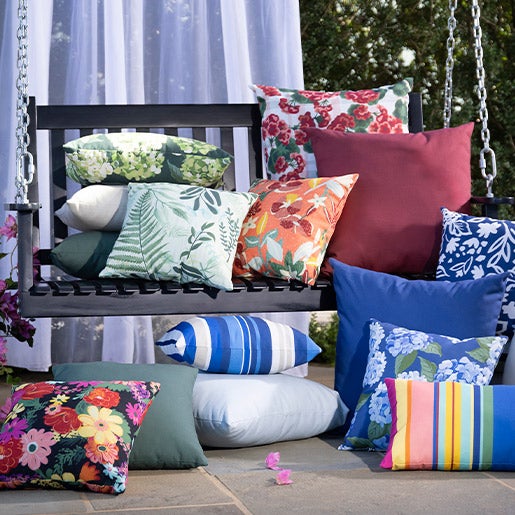 A stack of colorful outdoor throw pillows in stripes and patterns on an outdoor swing with outdoor curtain hanging behind