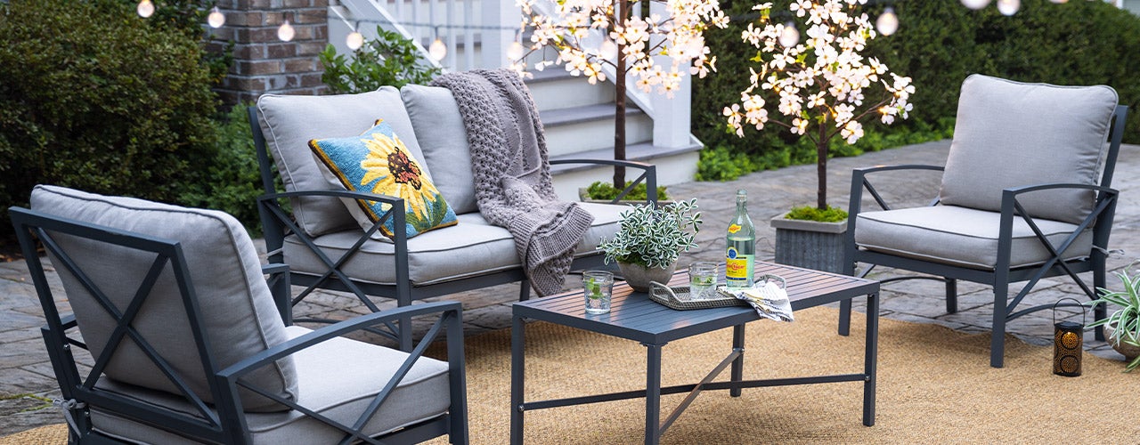 Plow & Hearth Outdoor Furniture. Image of the Arlington aluminum seating set with soft gray cushions on a patio with string lights.