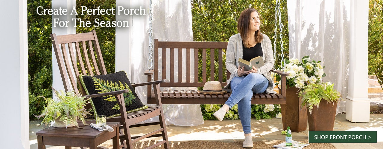 A woman sits on a wooden porch swing on a porch with white curtains. Create a perfect porch for the season. Shop Front Porch >