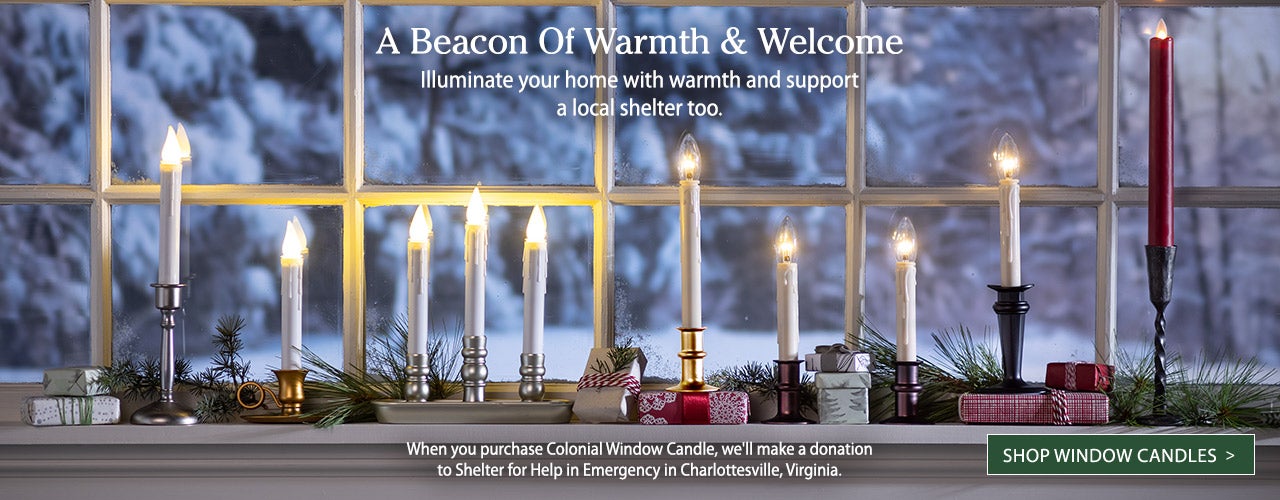 Image of assorted window candles in window lit up at night. A Beacon Of Warmth & Welcome. Illuminate your home with warmth and support a local shelter too.