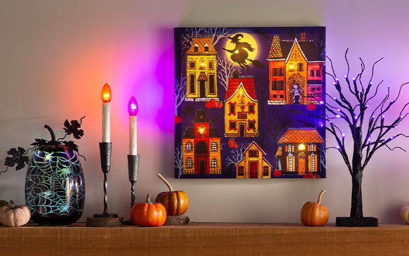 A mantel is decorated with lighted candles, pumpkins and lighted wall decorations