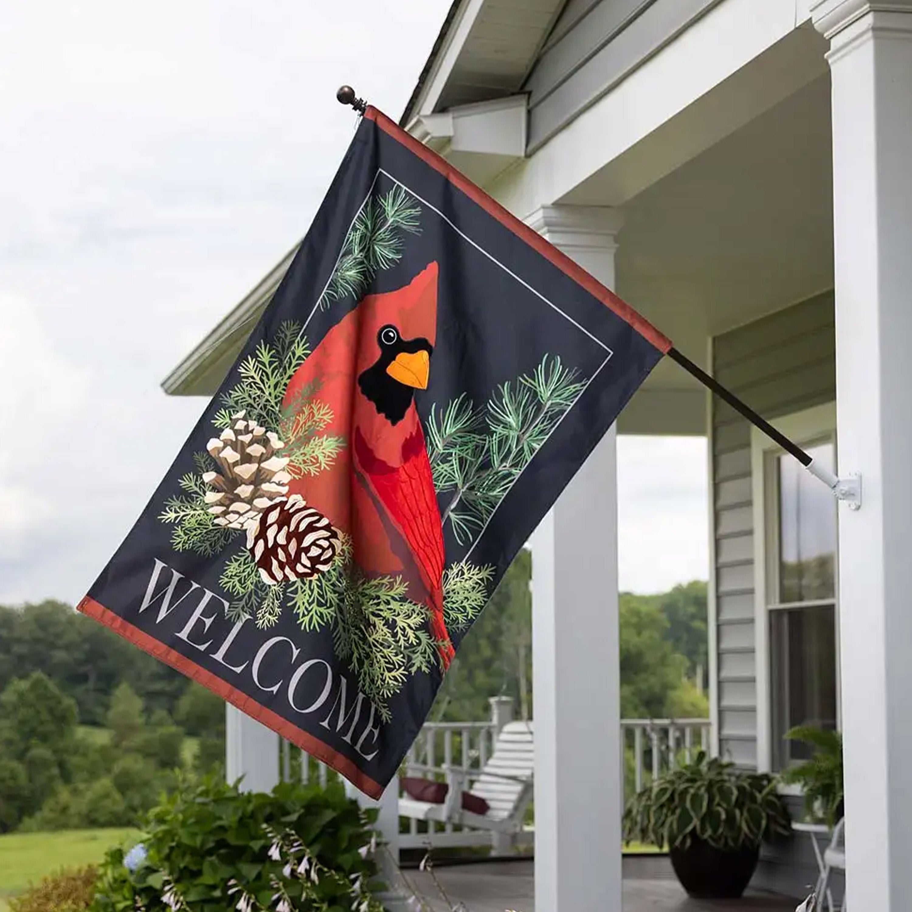 A large cardinal on pine boughs house flag hangs from a porch