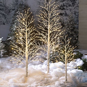 A trio of lighted faux birch trees in a snowy yard