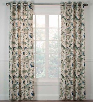 A window with grommet-top curtains with a Jacobean floral pattern in greens and blues.