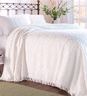 A bed with a white tufted chenille bedspread with a wedding ring pattern.
