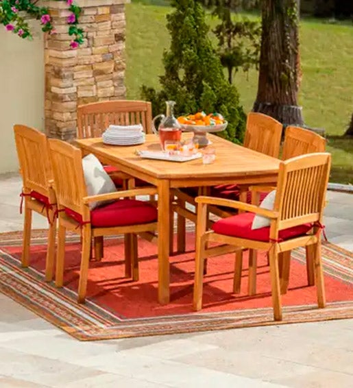 WOOD FURNITURE > Image of a teak wood dining set with floral cushions on a bright striped outdoor rug.