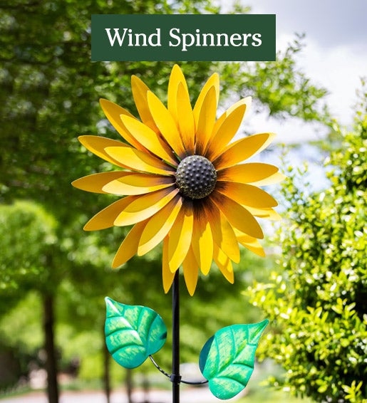 Bright yellow sunflower wind spinner with green leaves in a garden.