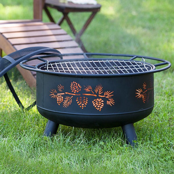 Pine Cone Wood Burning Fire Pit in Black outdoors on grass with adirondack lounge chair