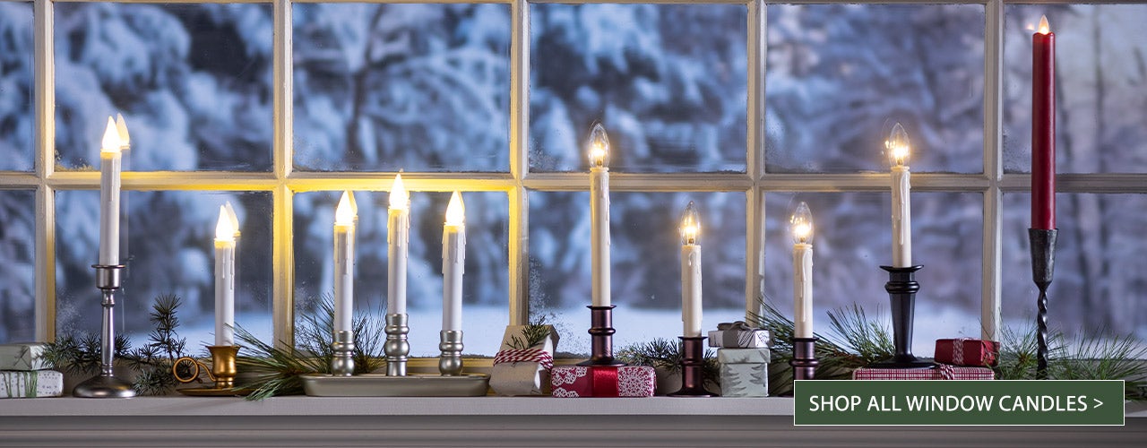 A wintery windowsill at night with a variety of battery-operated Christmas window candles - SHOP ALL WINDOW CANDLES>