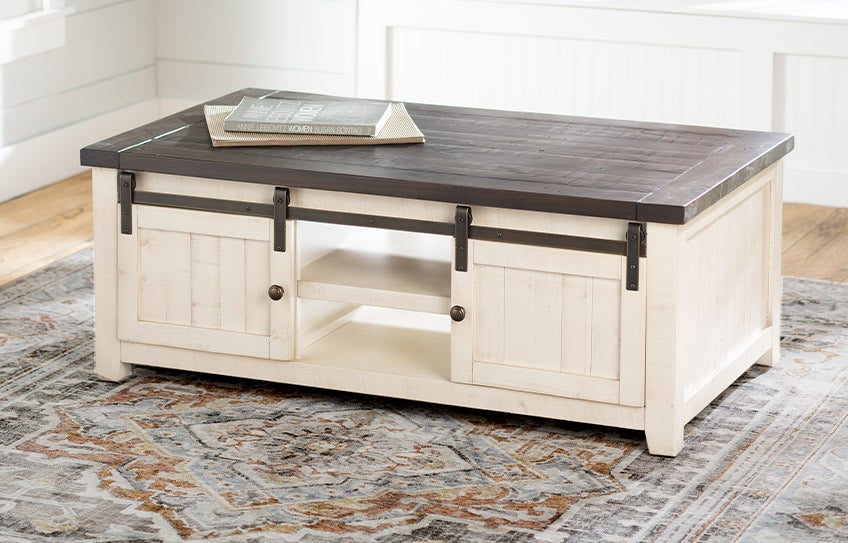 A Cape Charles farmhouse coffee table with barn door style doors and a distressed wood top.