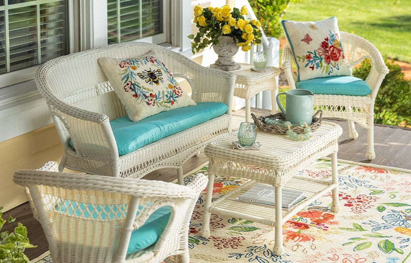 An Easy Care white wicker seating set on a front porch with floral accent cushions on an outdoor floral rug.