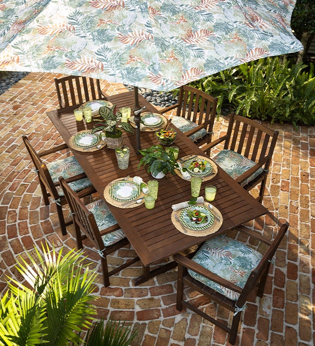 Lancaster eucalyptus wood dining set with a patio umbrella, cushions and summer place settings on a brick patio.
