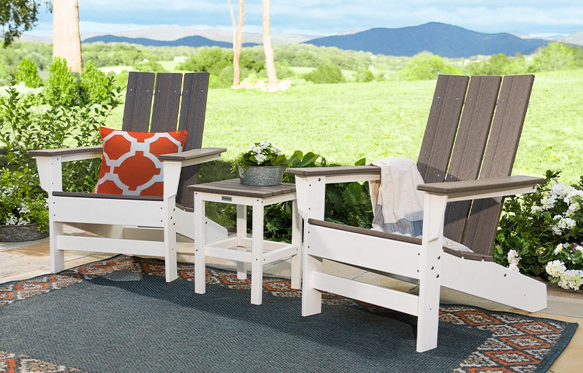 Two May River Collection all-weather Adirondack chairs and a side table in gray and white on a back patio.