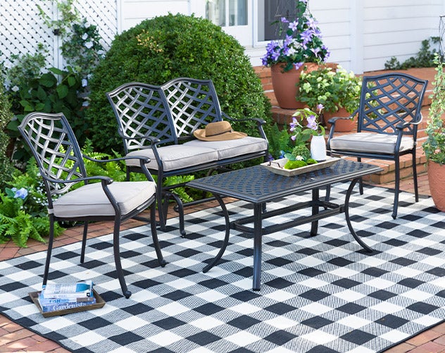 A Park Grove cast aluminum outdoor seating set with tan cushions on a buffalo check outdoor rug.