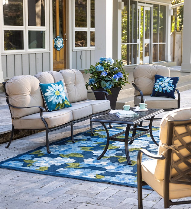 A Park Grove cast aluminum outdoor deep seating set with thick tan cushions and hydrangea accent pillows on a blue hydrangea rug.
