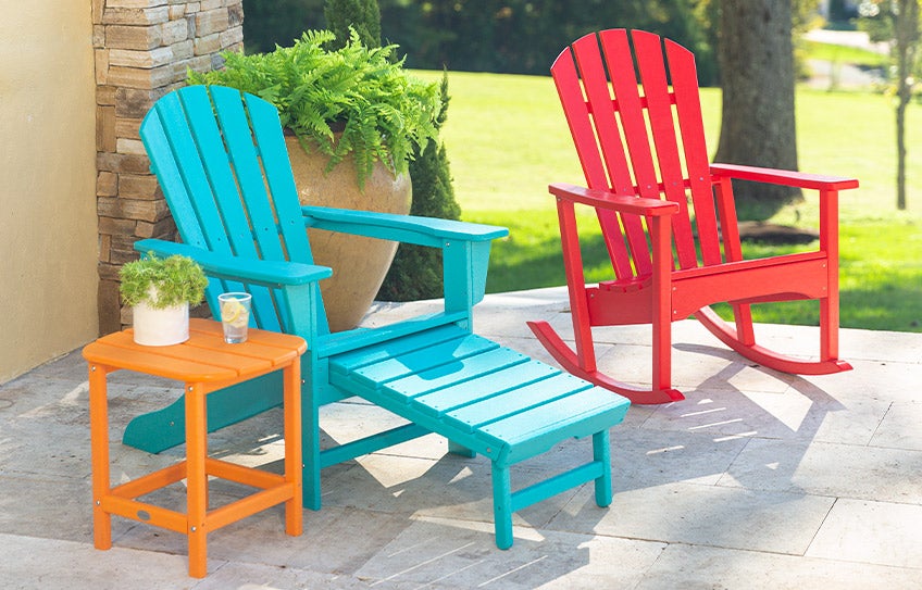A back patio scene of an Adirondack chair, rocker and side table in bright colors made of recycled plastic POLYWOOD lumber.