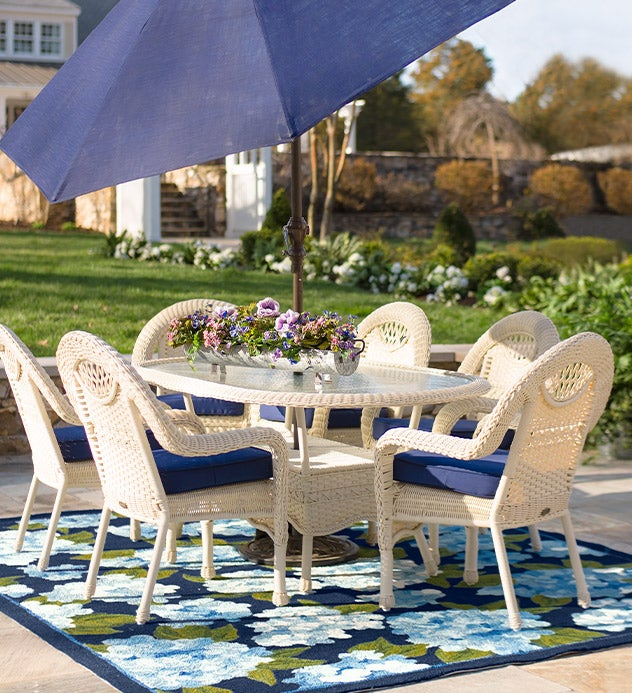 Prospect Hill oval dining table and six chairs in white all-weather wicker with deep navy cushions and patio umbrella.