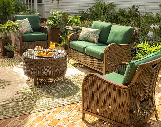 An Urbanna wicker seating set in brown with green cushions and leaf pattern accent pillows and rug.